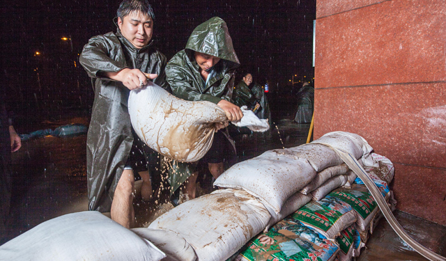 图为7月19日，河南滑县电力员工在110千伏文明变电站外顶着暴雨进行防涝作业。