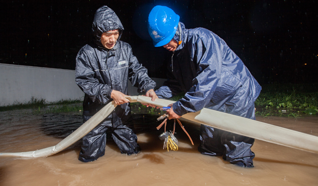 图为7月19日，河南滑县电力员工在110千伏文明变电站外顶着暴雨进行防涝作业。