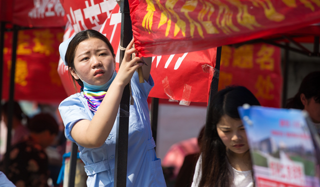 图为6月7日，考点外一名女医护人员忙着悬挂自己的宣传横幅。